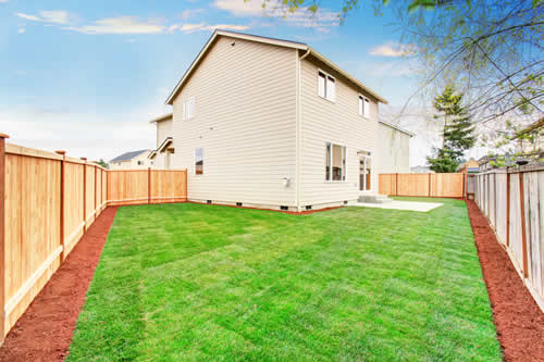 Fenced in backyard with beige house in the background